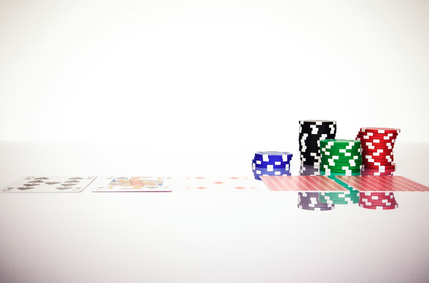 Carte da gioco e fiches da poker disposte ordinatamente su una superficie bianca.