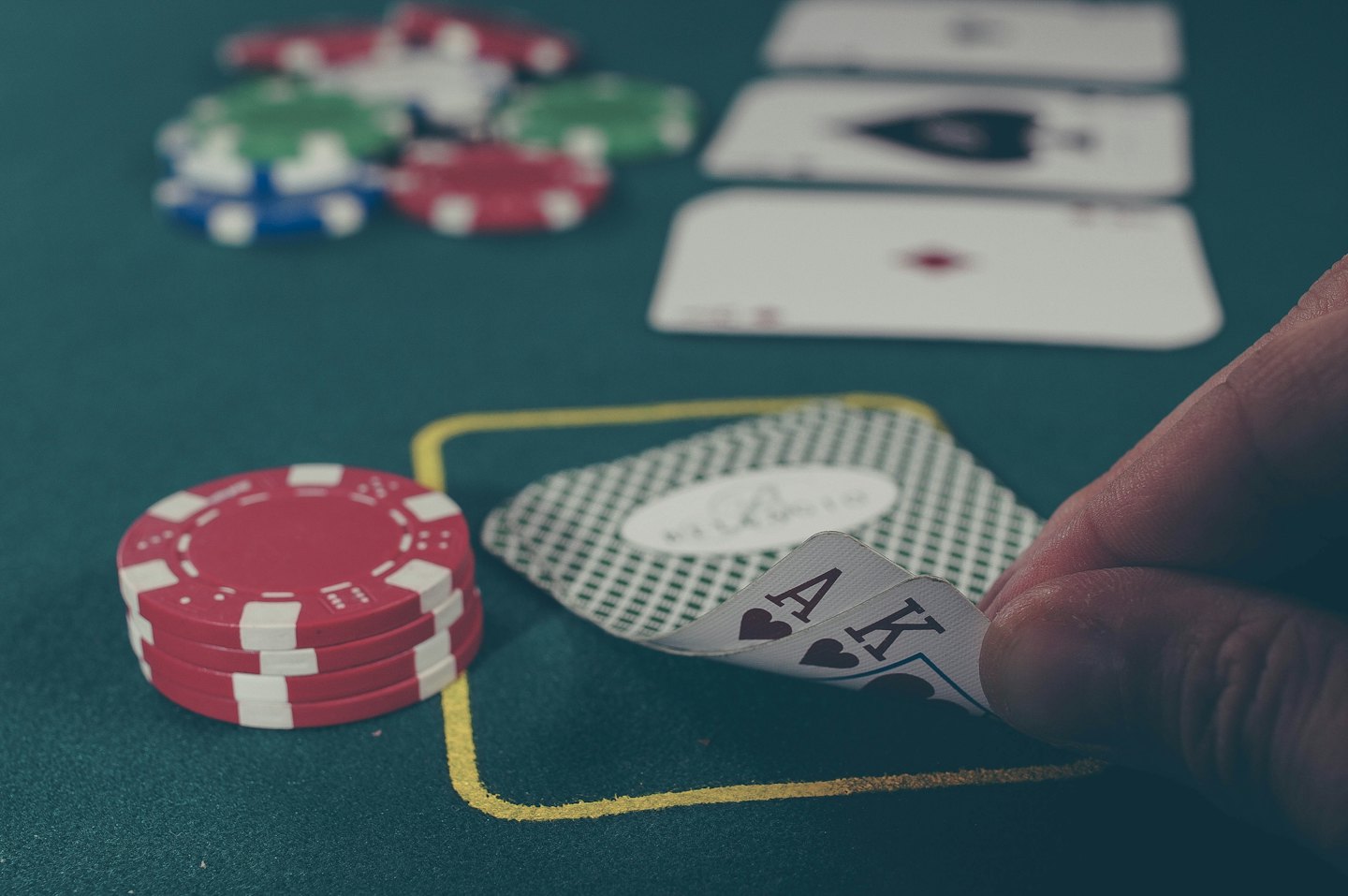 Mano che tiene Asso e Re di cuori su un tavolo da poker.